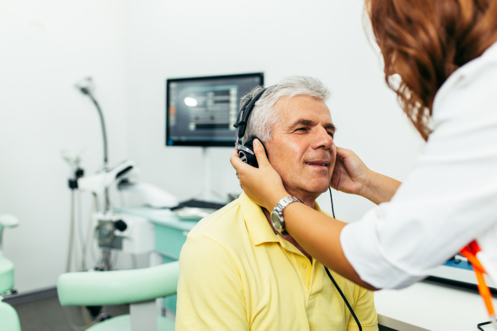 monsieur d'environ 60 ans qui réalise un dépistage auditif appelée "une audiométrie" par une professionnelle de l'audition